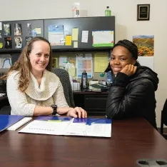 Two women sitting at a desk, looking over a folder together at Student Support.